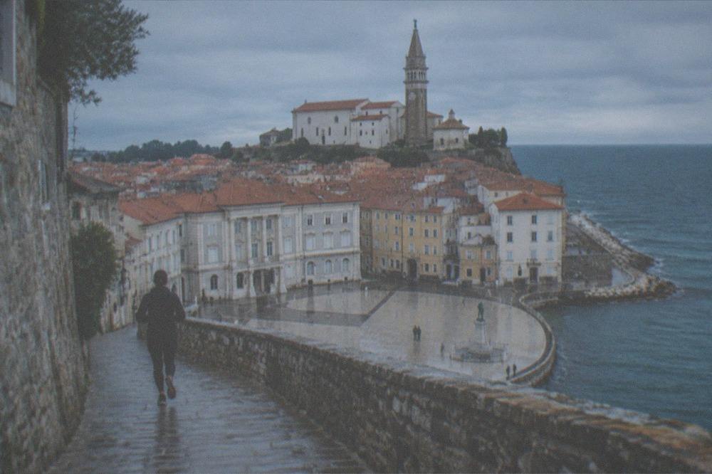 A stone bell tower rising above red rooftops toward a blue sea horizon.