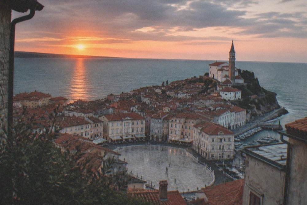 The sun setting over a coastal peninsula town with the sea reflecting orange light.