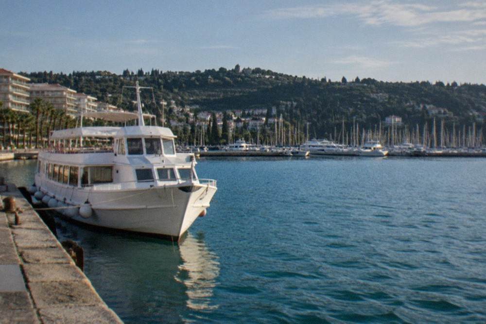 A white coastal passenger boat moored at a small stone quay with hills behind