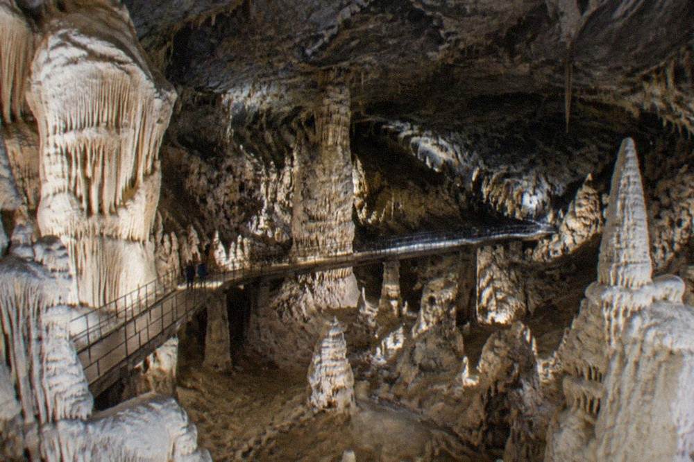 A white castle built into a cliff face with a cave mouth opening beneath its walls