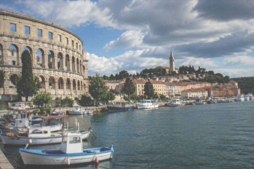 A hilltop church above a harbour town with fishing boats moored along the waterfront