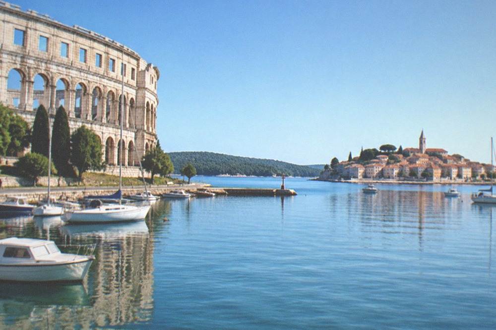 A small stone town on a peninsula with terracotta roofs reflected in calm sea