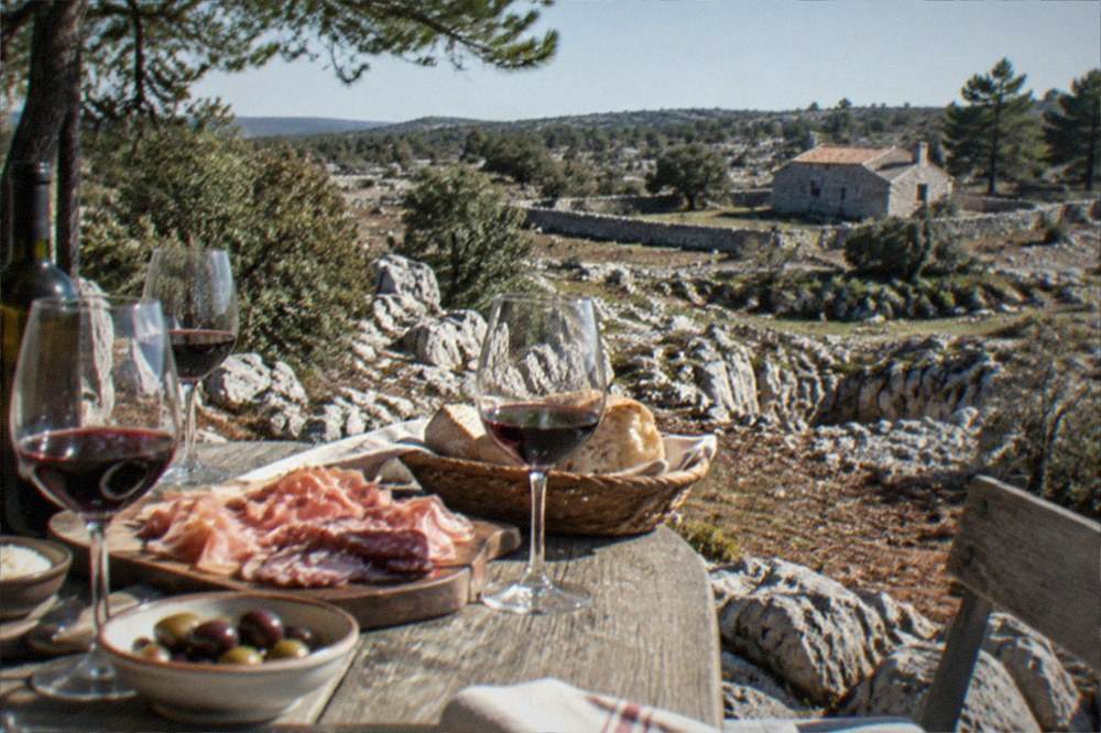 A rustic Karst farmhouse table set with wine glasses, cured meats and bread