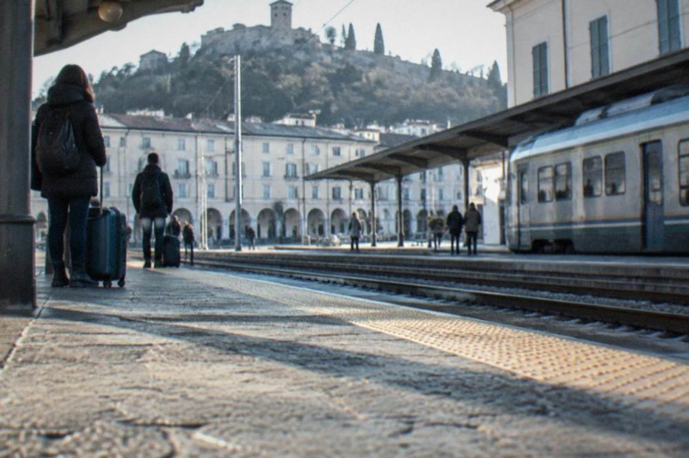 Regional train platform with a station building and passengers waiting with luggage