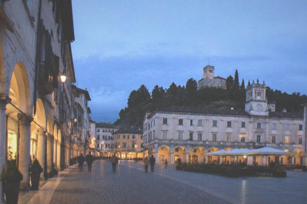 Cobblestone shopping street in Udine lined with old buildings and small shops