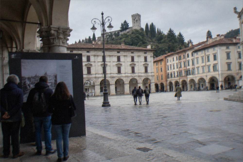 Travellers reading a museum entrance sign beside a ticket window in an Italian city