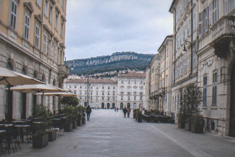 A quiet morning street in central Trieste with even paving and café tables on the level sidewalk