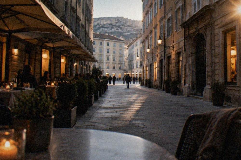 An evening restaurant terrace in a narrow old town street with lit windows