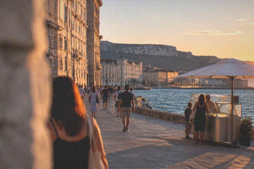 A seaside promenade at dusk with people walking past a gelato stand