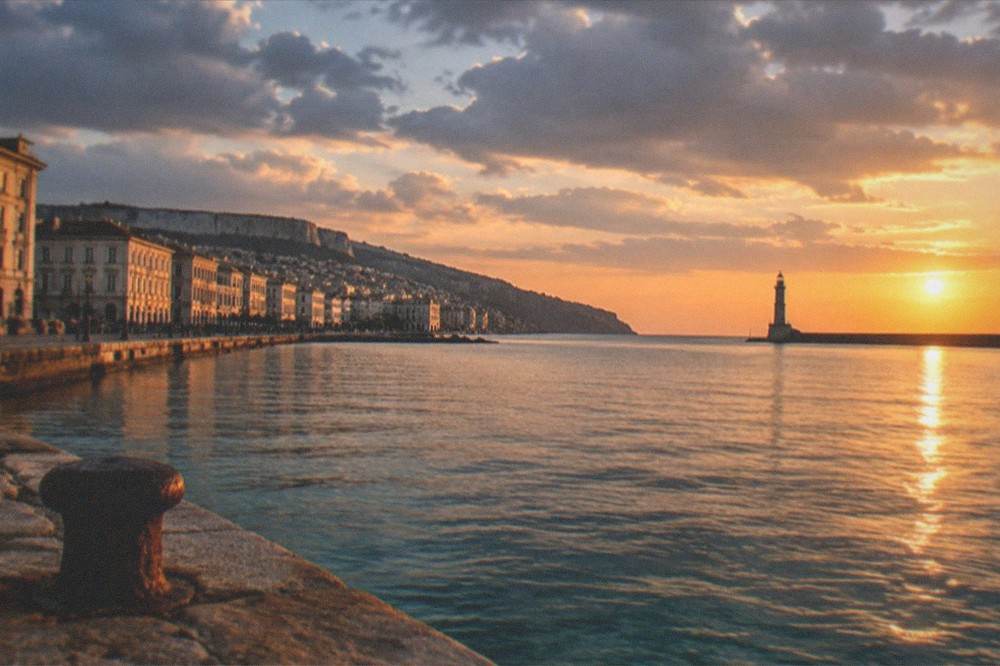 The waterfront of Trieste at sunset with the lighthouse silhouette and calm sea