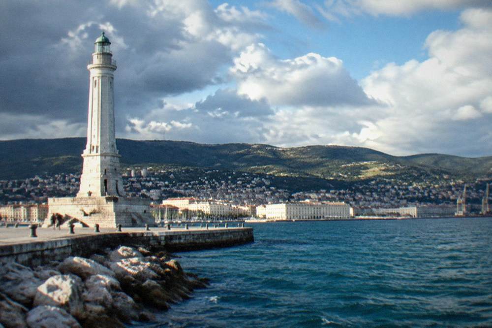 The Faro della Vittoria lighthouse in Trieste seen from the mole with the seafront curving away behind it
