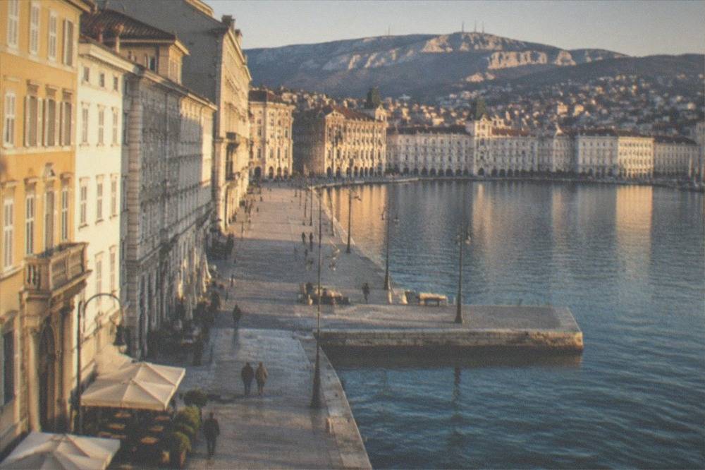 The skyline of Trieste seen from Molo Audace at dusk with Piazza Unità d'Italia lit across the water