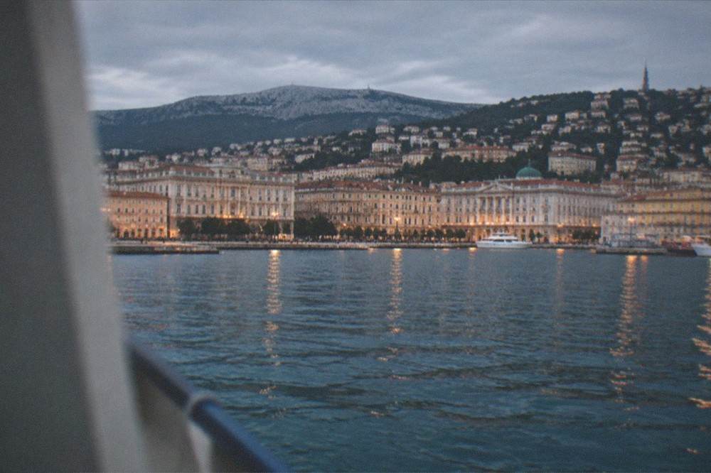 Evening view of Trieste's seafront and hillside from the water with the city lights beginning to come on