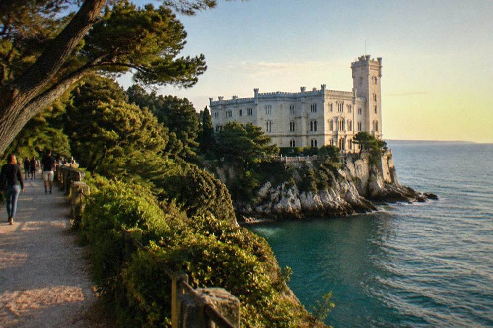 Visitors walking on a gravel path through the wooded park above the sea at Miramare