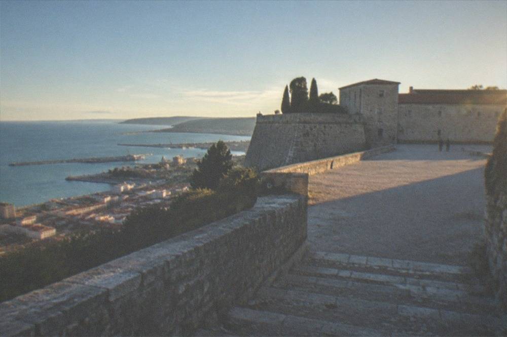 A stone staircase leading up to the walls of Castello di San Giusto in the late afternoon