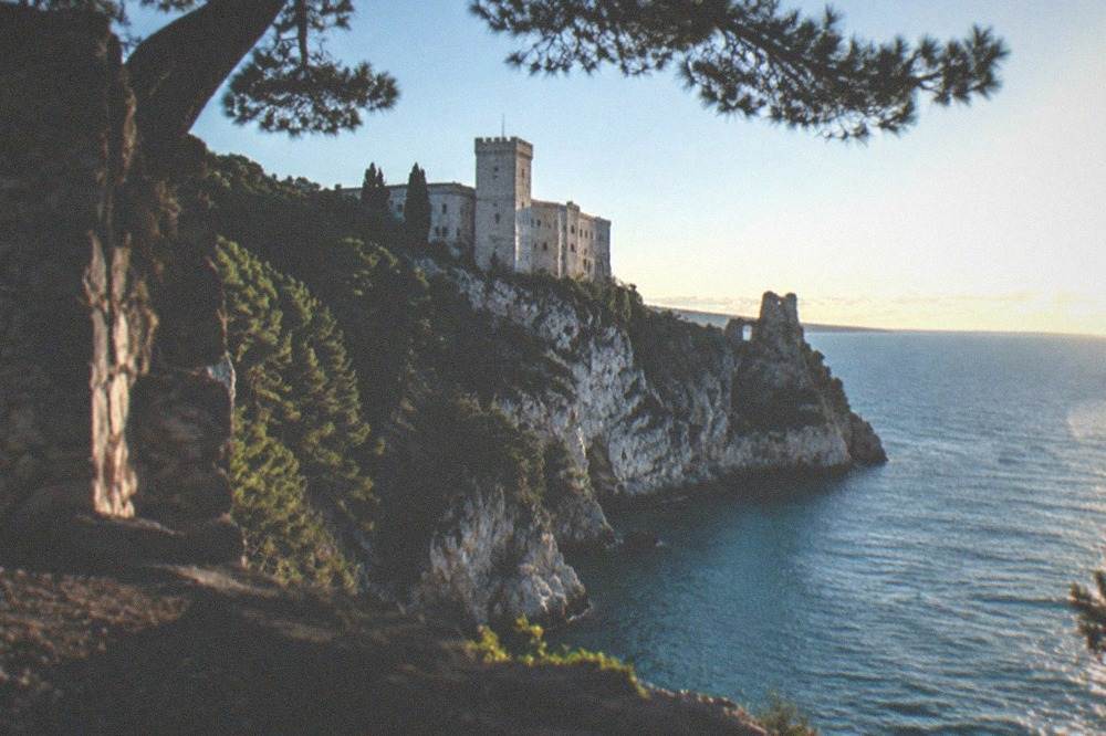 The cliffs and ruined tower of old Duino Castle above the blue water of the Adriatic