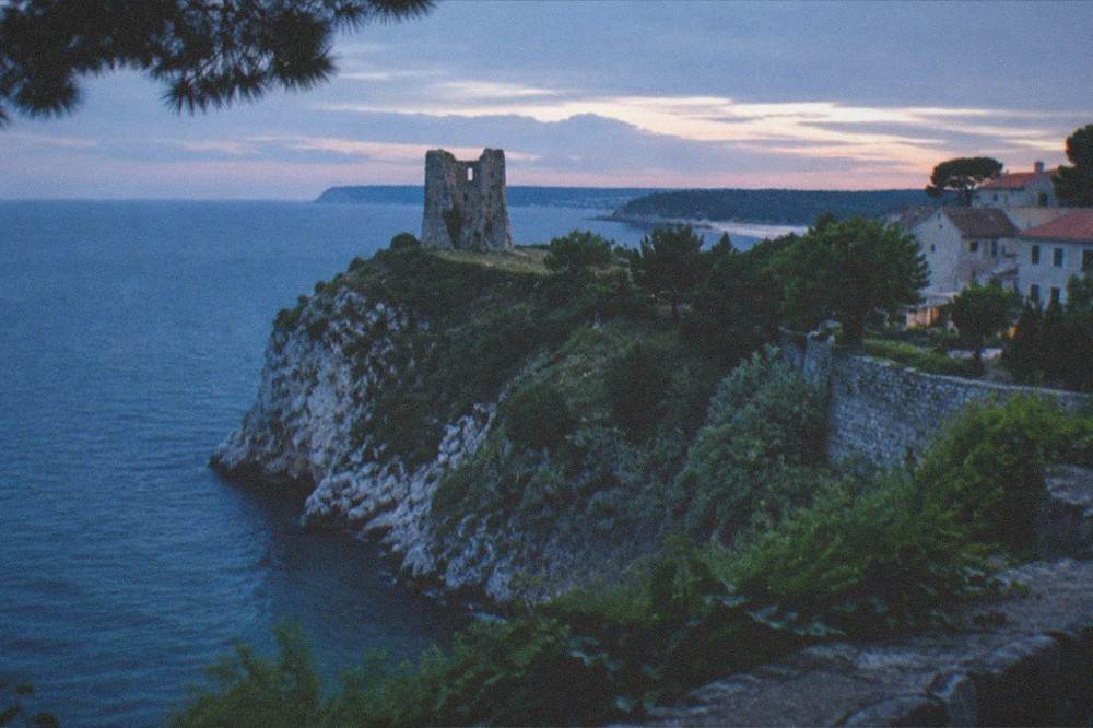 An old stone tower ruin on a grassy cliff above the sea near Duino
