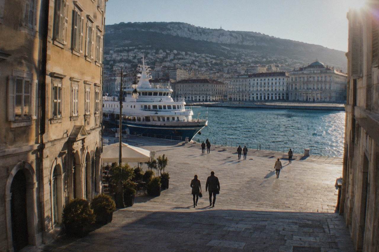 A passenger ferry moored at a quay in the port of Trieste with the city waterfront behind it