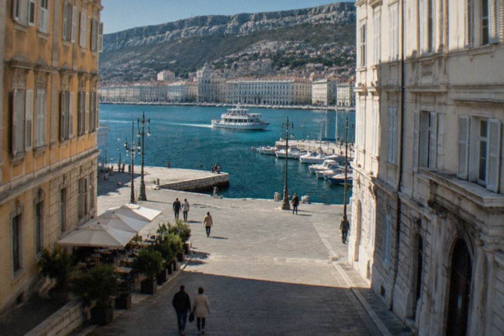 Small boats and an excursion vessel at a stone quay on the Trieste seafront in morning light