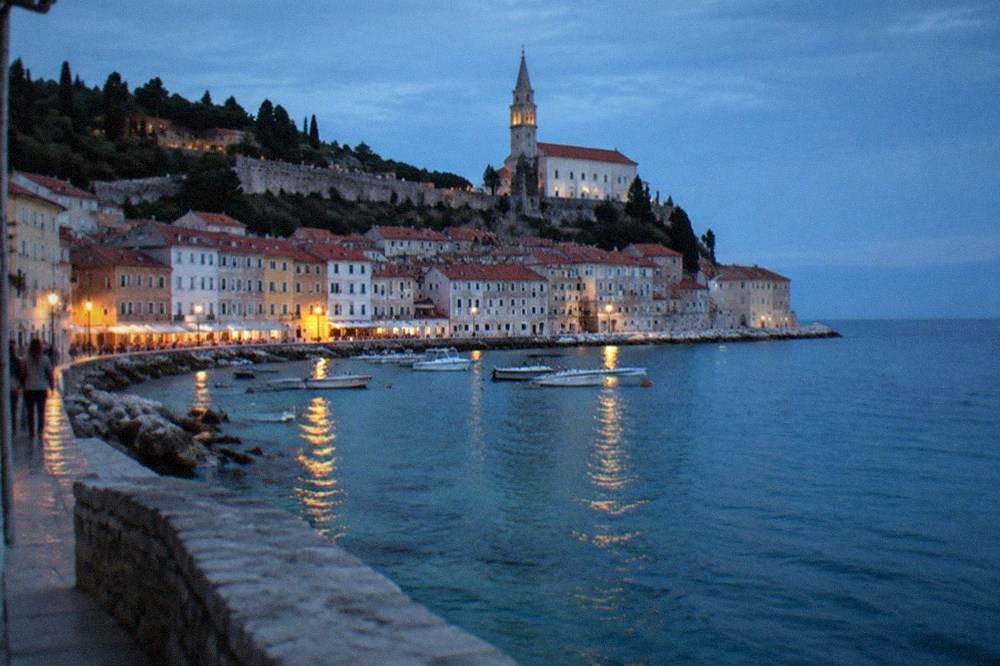 A border-sign style view of the rocky coastline near Piran with small boats in a harbour