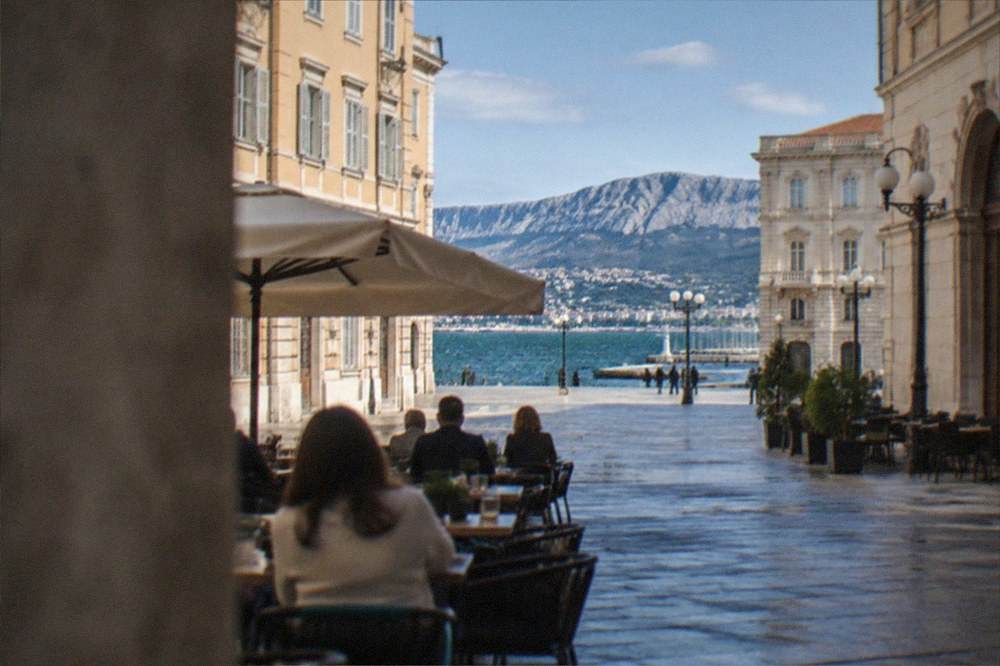 People seated at outdoor tables on a historic square in central Trieste