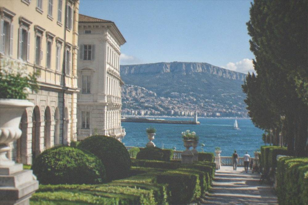 A manicured garden avenue with sculpted hedges and a view of the sea between the trees