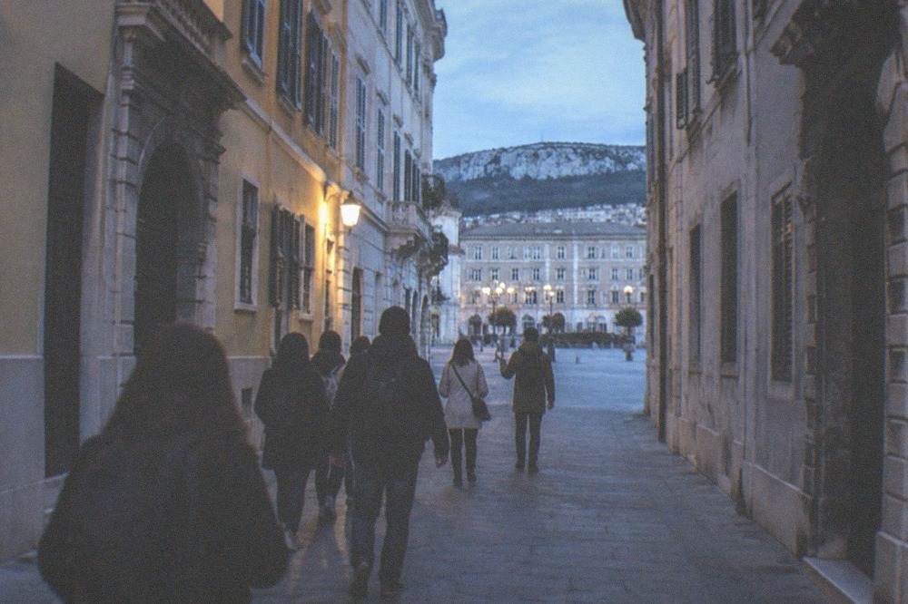 A small group of walkers following a guide down a narrow old-town street lined with tall shuttered buildings