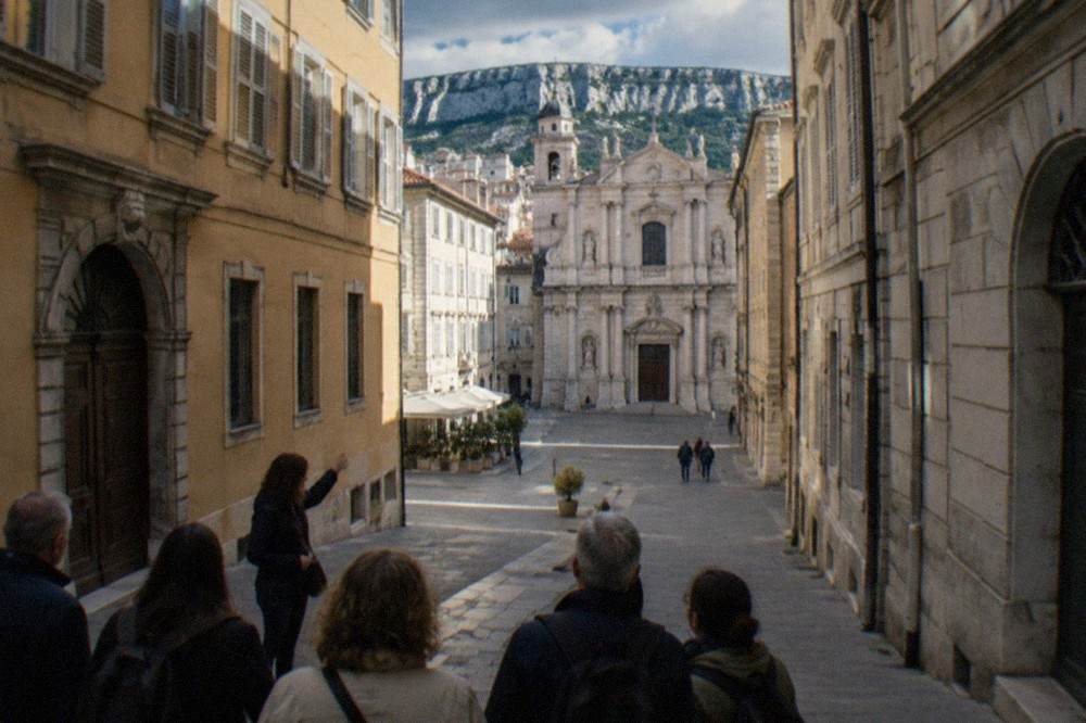 A tour guide gesturing towards a baroque church facade while a small group listens in a narrow Trieste street