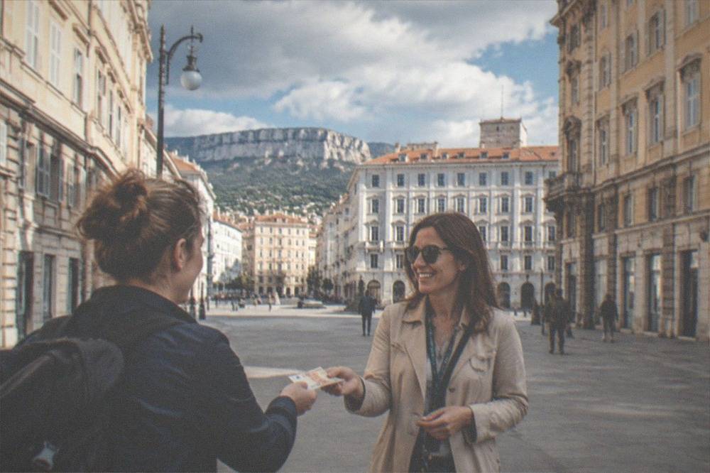 A visitor handing euro banknotes to a smiling tour guide at the end of a city walk