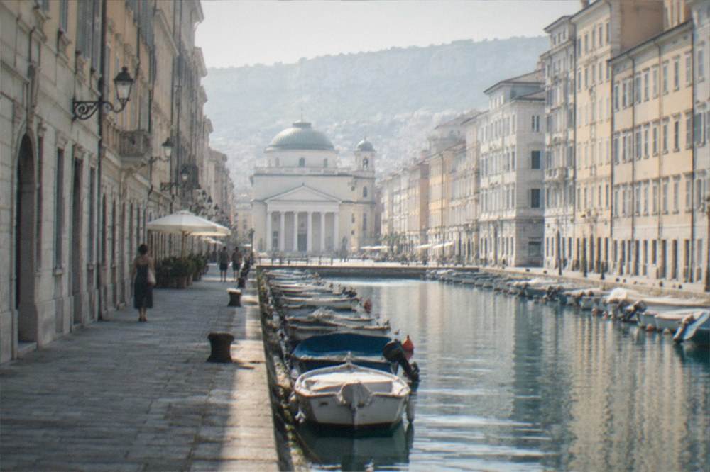 A quiet canal-side street in Trieste with a church at the far end and small boats moored along the water
