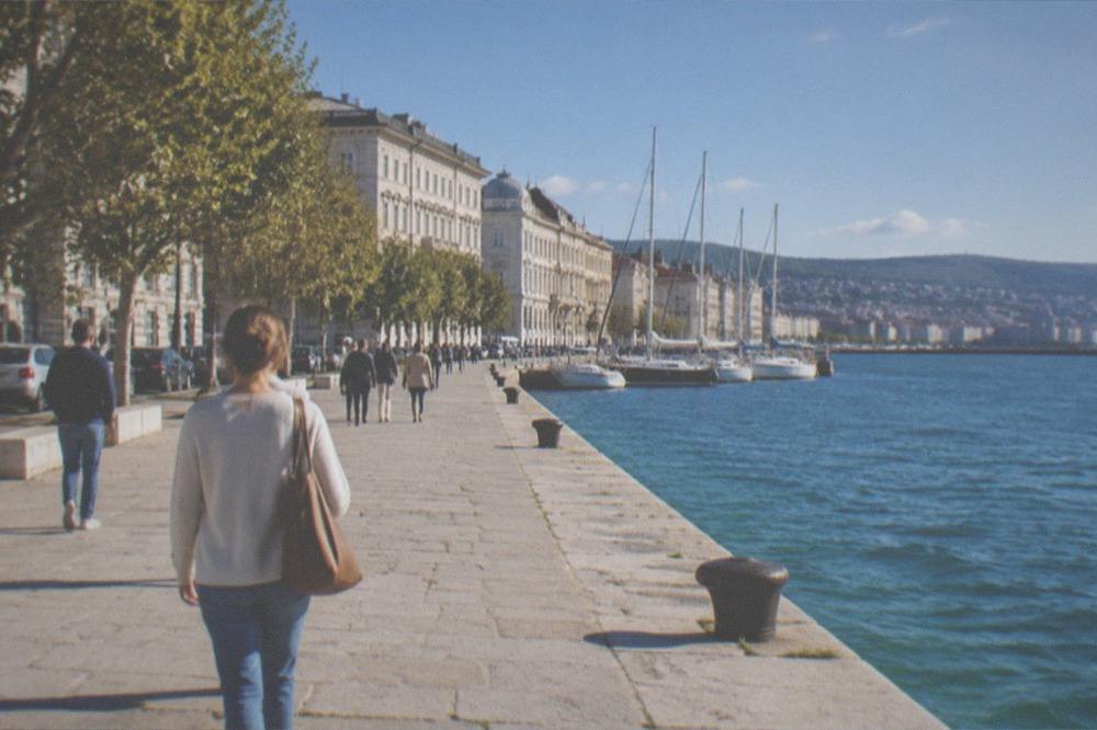 A wide seafront promenade in Trieste with people walking and the coastline curving away