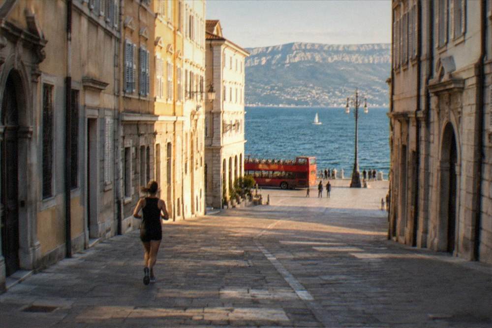 An open-top sightseeing bus parked on a Trieste square with the sea in the background