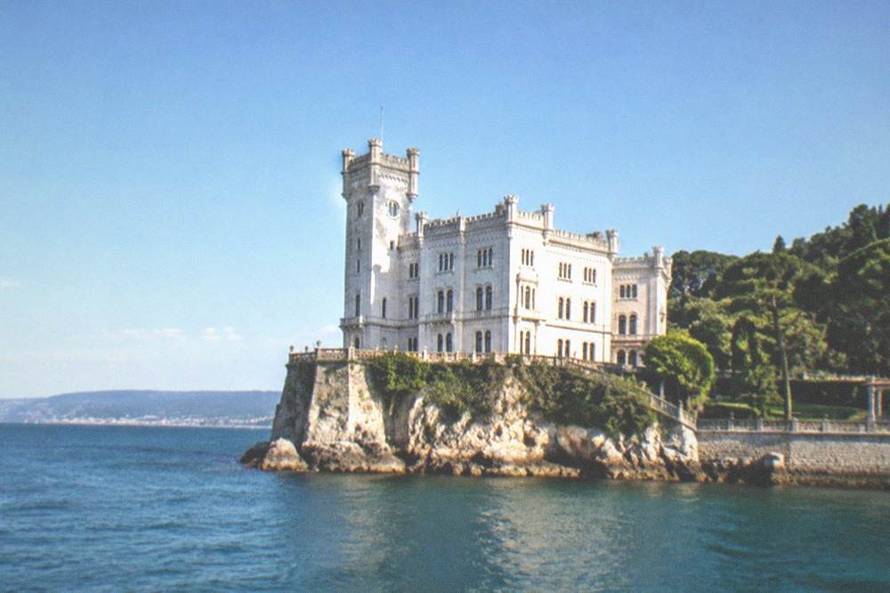 The white facade of Miramare Castle above its park near the sea