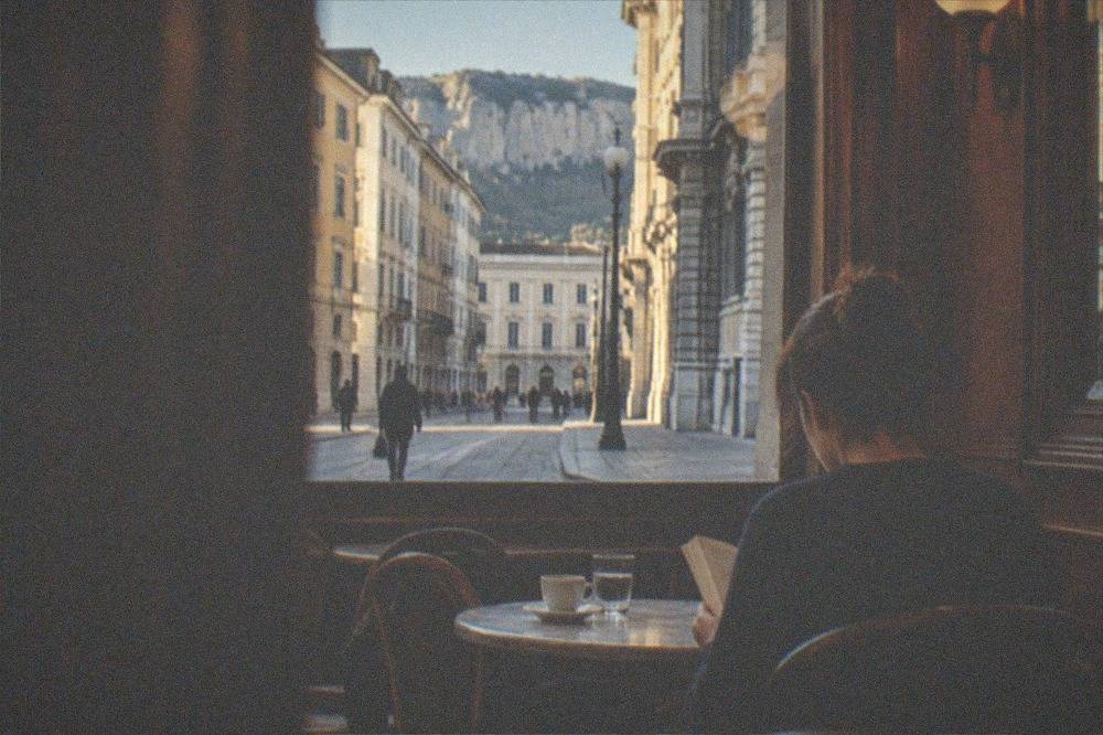 A reader sitting alone at a marble table inside a wood-panelled historic Trieste caffè