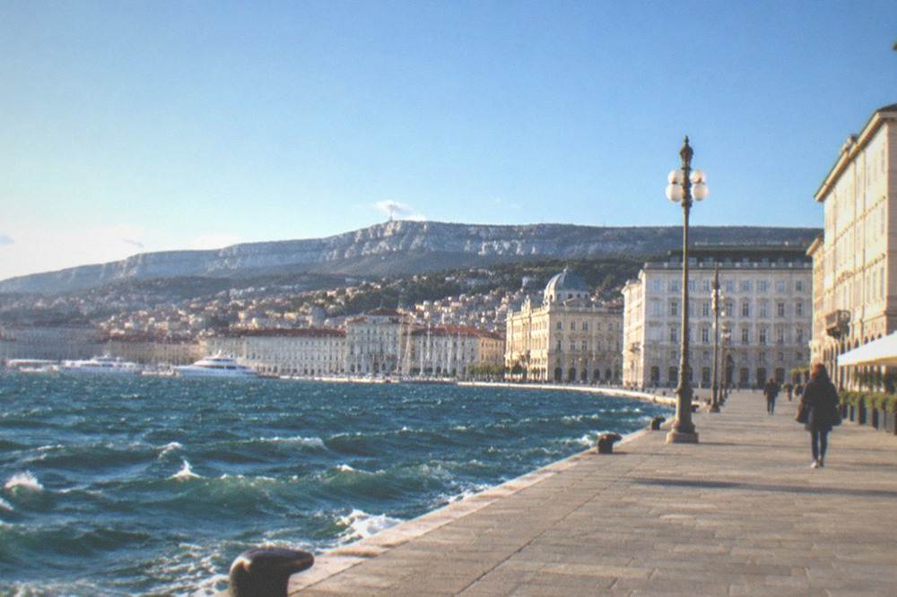 Whitecaps on the Gulf of Trieste seen from the seafront with the city skyline behind and flags straining in the wind
