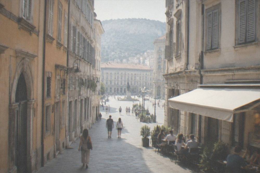 A narrow lane in Trieste's old town with a small buffet storefront and people eating at outdoor tables