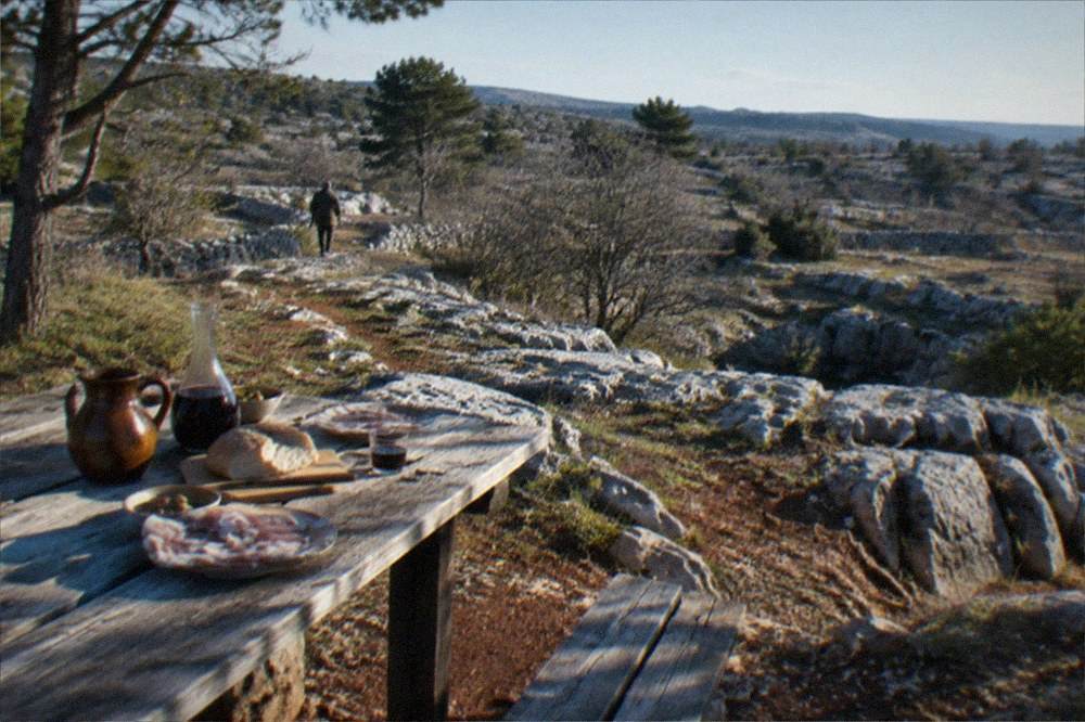 A rustic farmhouse table on the Karst plateau with jugs of homemade wine, bread and plates of cold pork