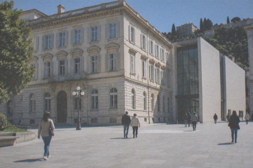 Visitors in light jackets walking a sunny European square between ornate buildings