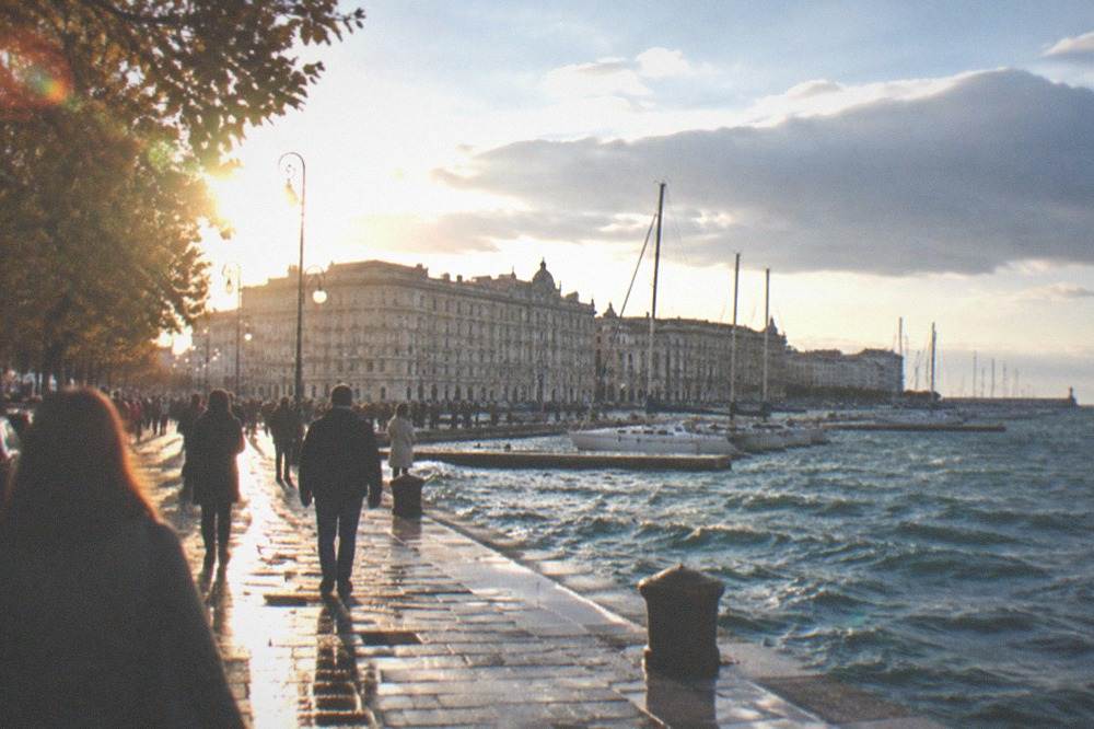 Sailboats moored along a seafront promenade with crowds of spectators on a bright autumn day