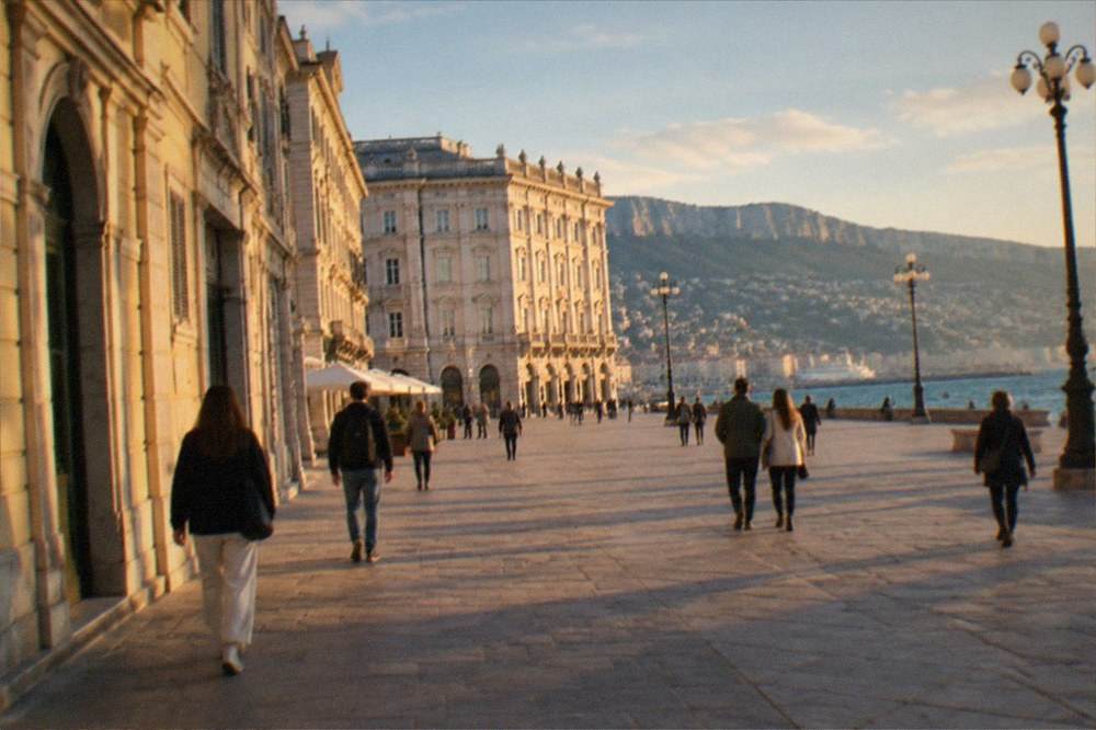 People walking across a grand seaside square with ornate facades and open sky