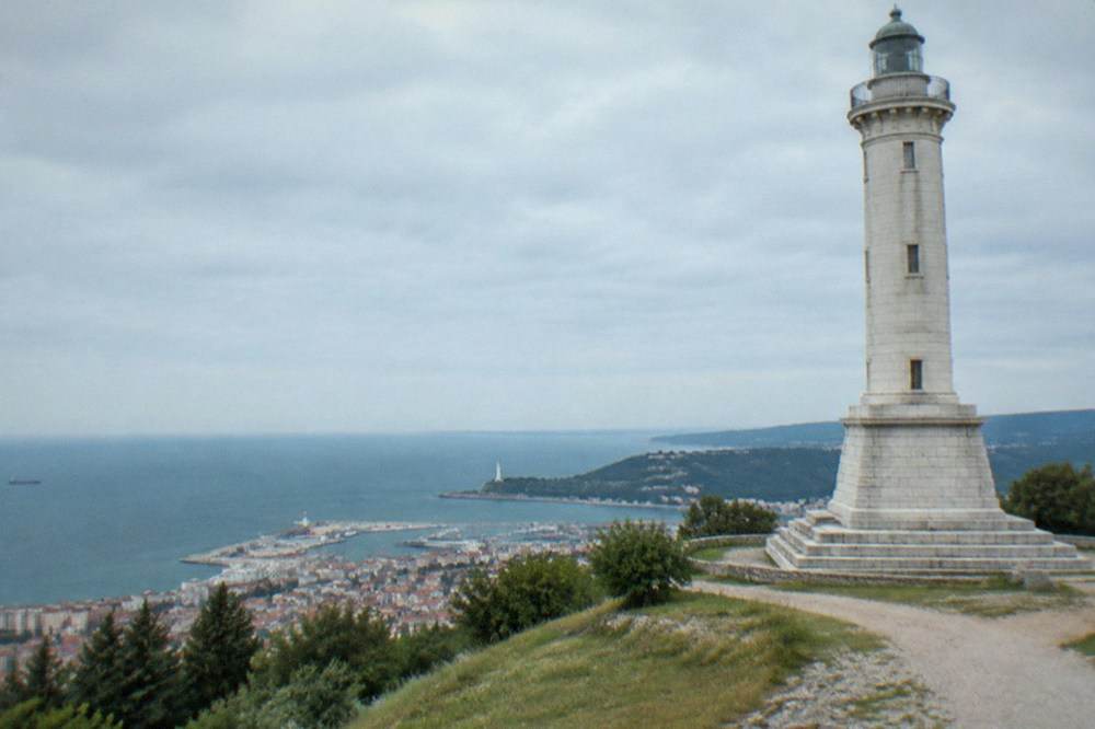 A calm morning sea along the Trieste gulf with the Faro della Vittoria lighthouse visible on the headland