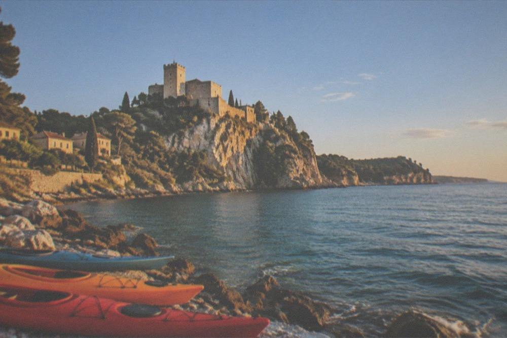 Kayaks resting on a rocky shore near Duino with a castle on the cliff above