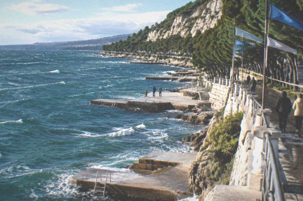 Whitecapped blue water in a gulf with flags straining in the wind along a promenade railing