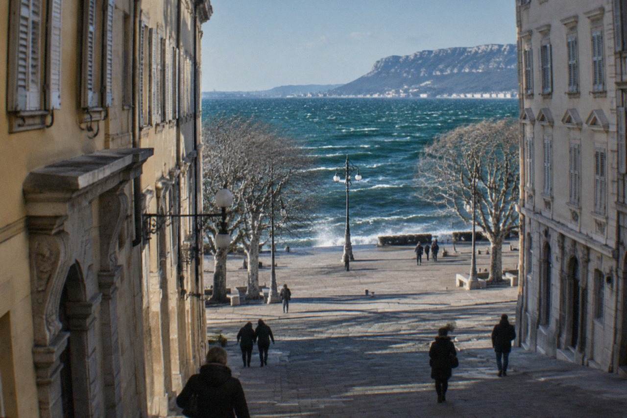 Whitecaps on the Gulf of Trieste under a clear windy sky, with the seafront and distant hills visible