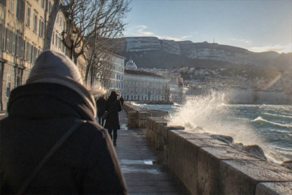 Spray blowing off a stone breakwater into bright clear air above a choppy sea