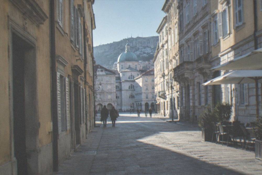 A narrow street in Trieste old town with pastel buildings and a church dome in the distance