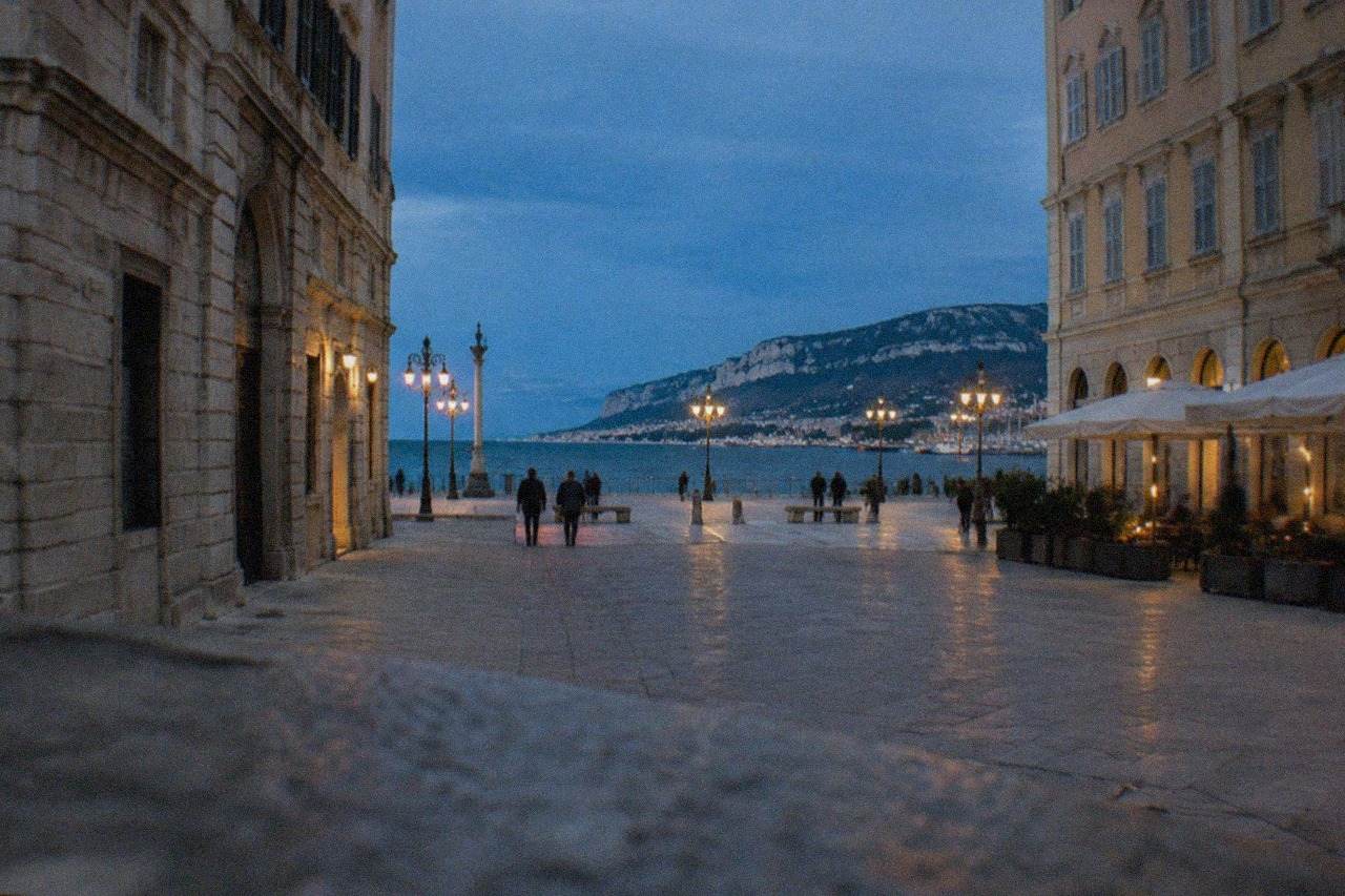 Evening view over a lit square in Trieste with the seafront beyond