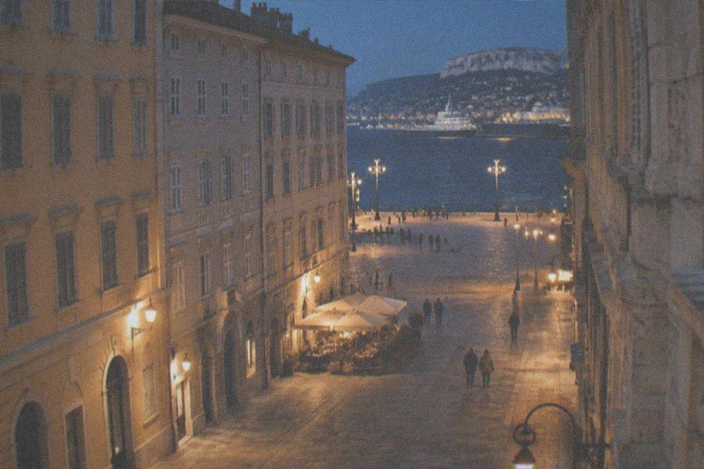 A lit street in central Trieste at night with the seafront promenade visible in the distance