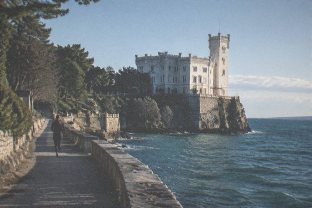 The white Miramare Castle above the sea on its rocky point near Trieste with the shoreline path below