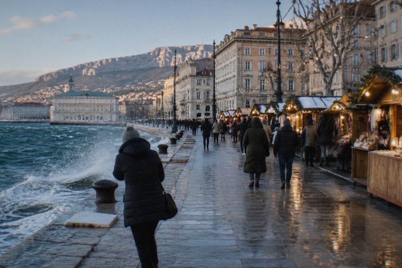 Festive market stalls and string lights along a seafront square in Trieste at dusk